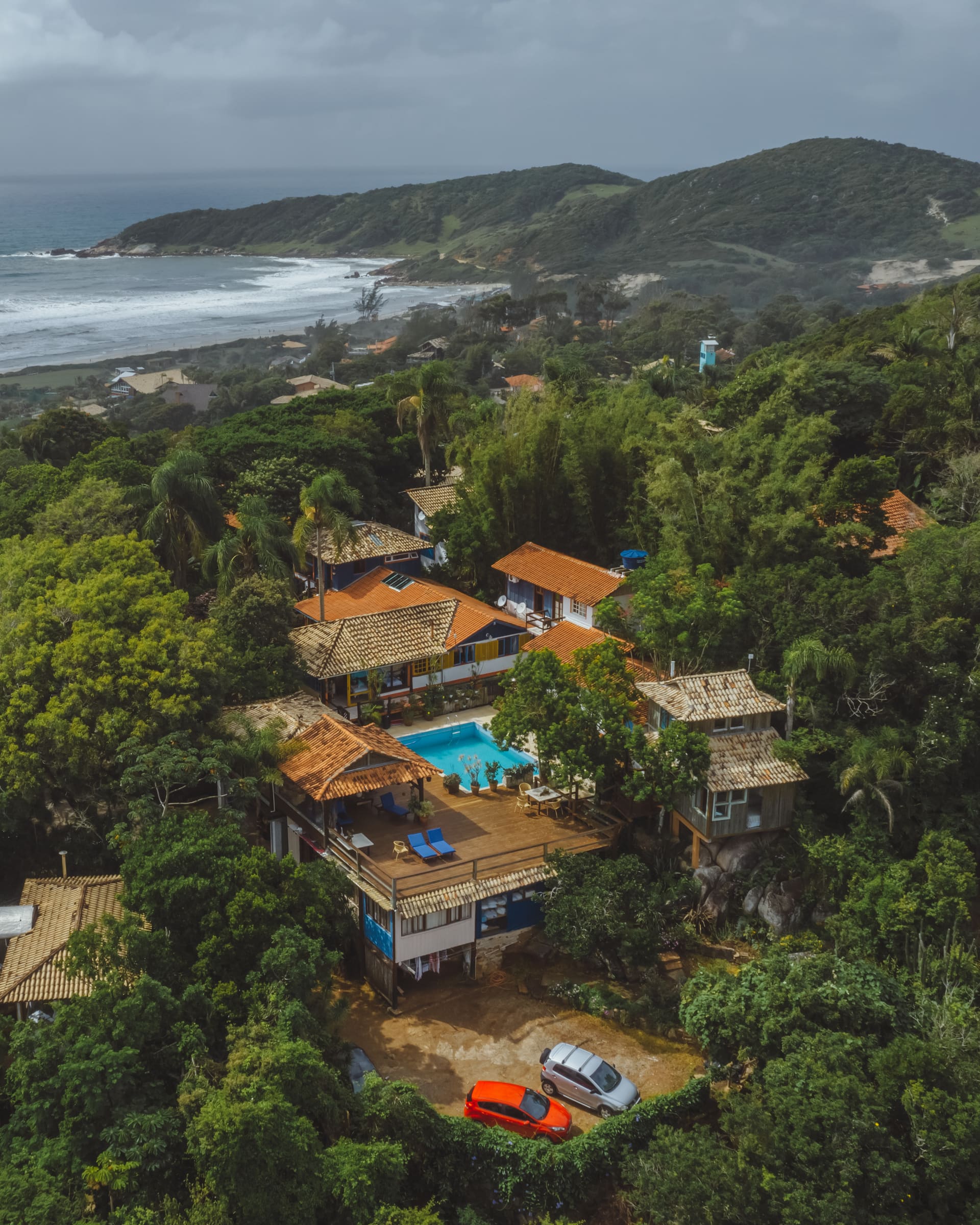 Vista aerea de pousada com piscina no litoral, mata e mar ao fundo.