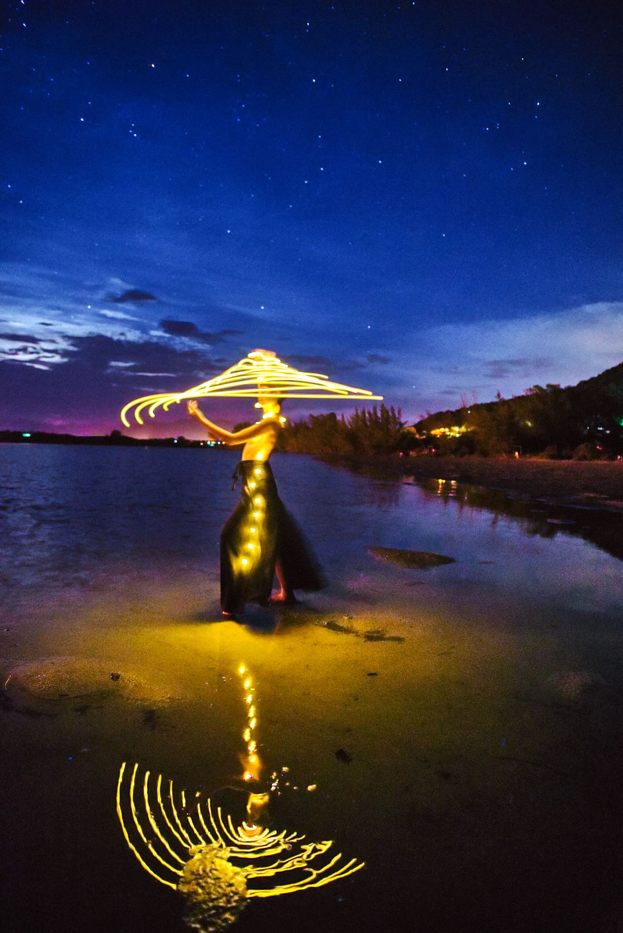 Light painting: figura dourada com sombrinha na praia ao anoitecer.