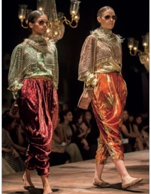 Duas modelos de Sabyasachi em calcas de veludo e brocado, sob lustres.