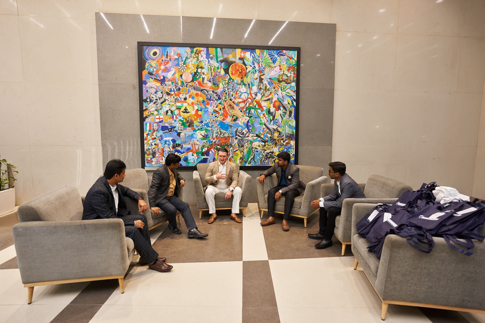 Reuniao de executivos em area de convivio, obra de arte ao fundo.